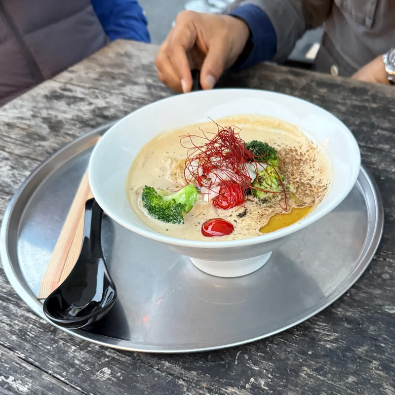 Bowl of Yuzu Coconut Cream Vegan Ramen served on a metal tray with wooden chopsticks and a black spoon