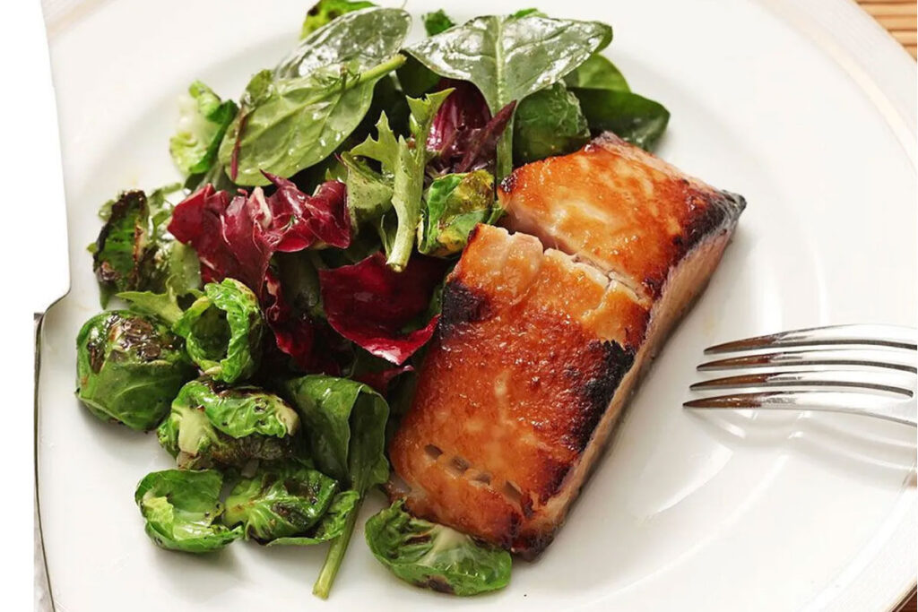 A white plate with a piece of miso-glazed cod and a side of Brussels sprouts and mixed greens.